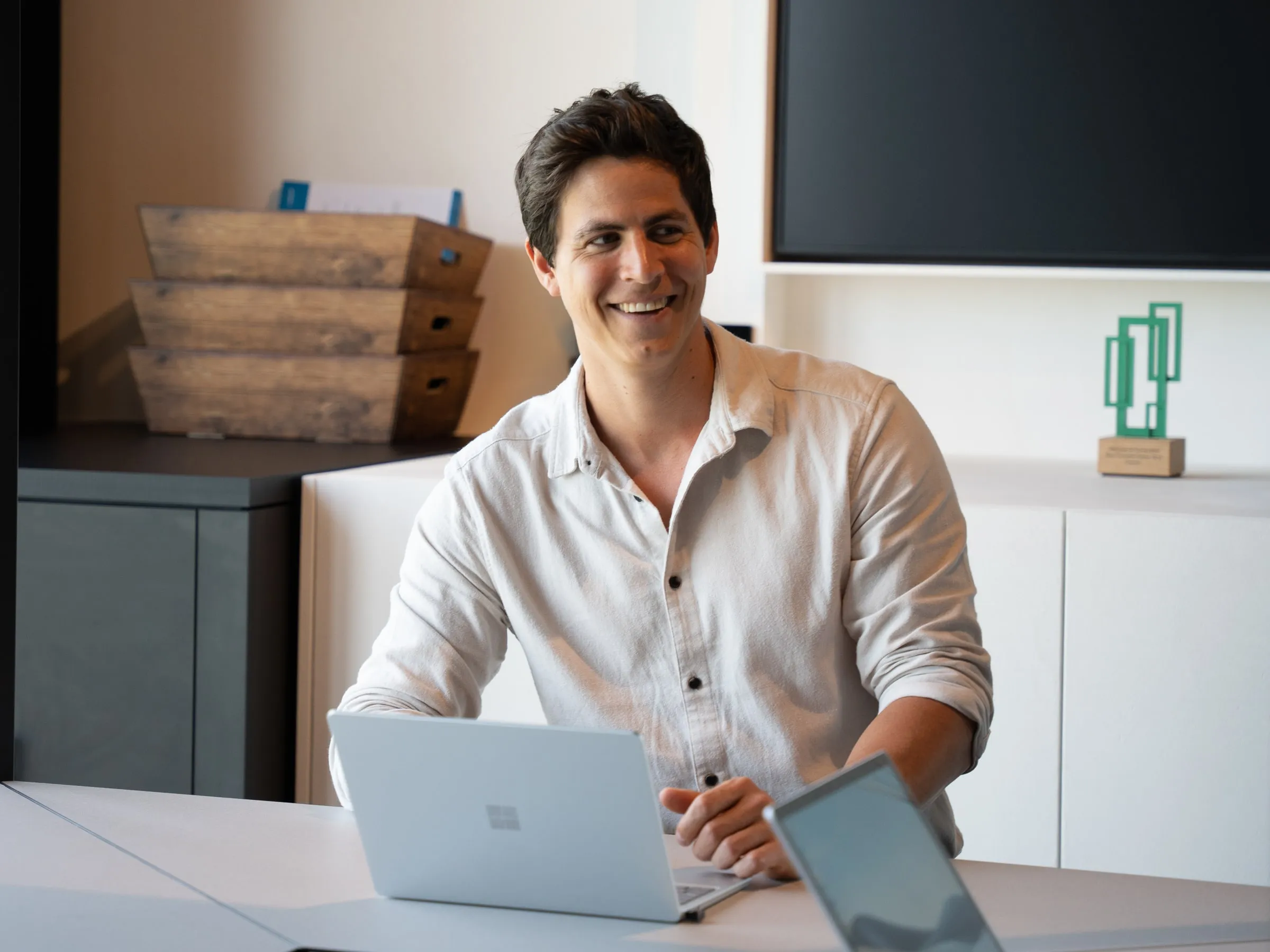 Nicolas aan zijn bureau met een laptop, lachend